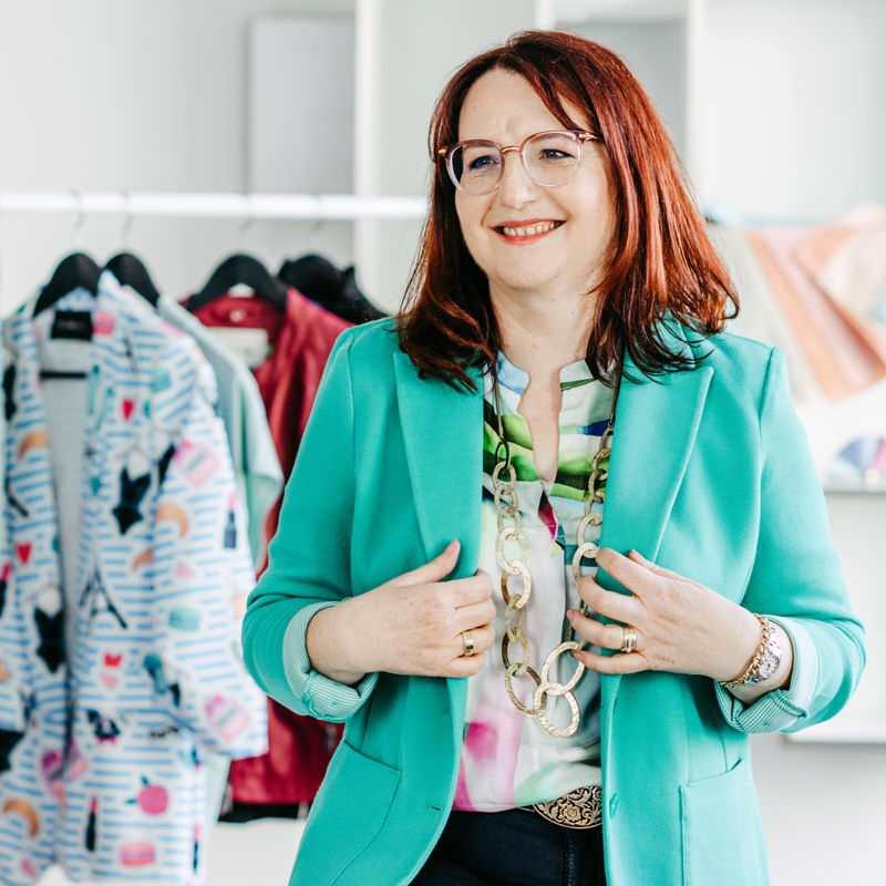 Jeanette vor einem Kleiderständer. Hält sich an Ihrem Blazer fest