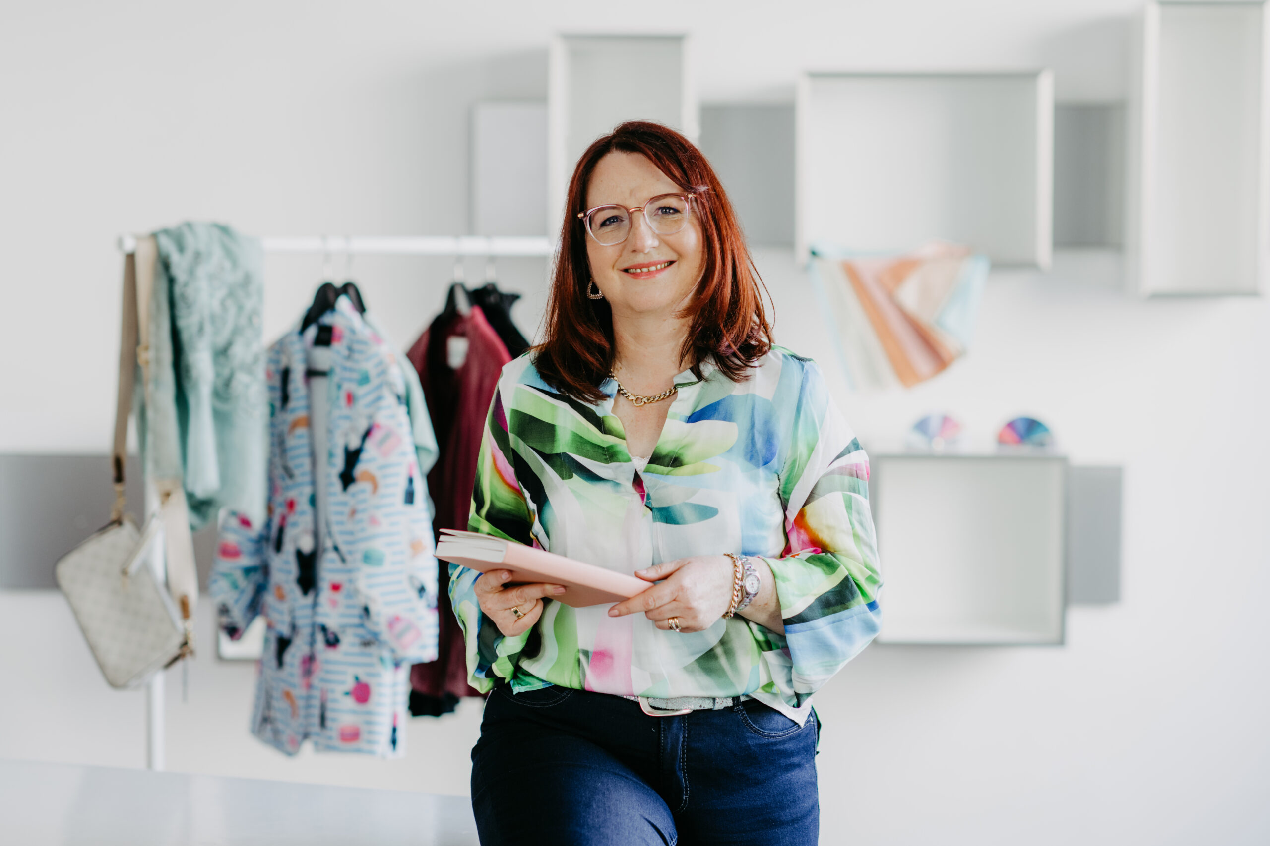 Jeanette Scheuernstuhl vor einem Kleiderständer sitzend mit Notizbuch, Stilberatung