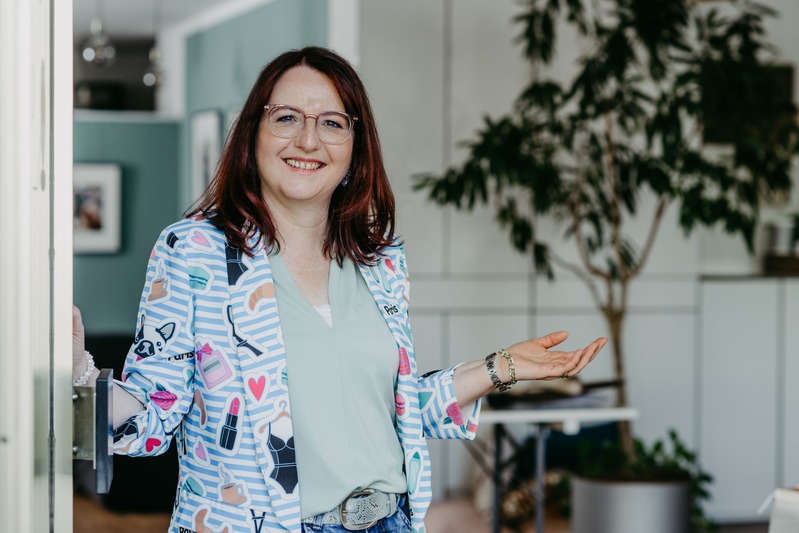 Jeanette Scheuernstuhl stehend an der offenen Ladentür begrüßend
